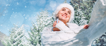 Happy smiling woman portrait in knitwear and fur hat enjoys with a hot cup of tea on sunny winter day during snowy forest walk.の写真素材