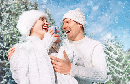 Middle shot of happy cheerful sincerely laughing Caucasian couple dressed knitted outfit clothes in the snowy winter forest.の写真素材