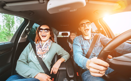 Cheerful young traditional family has a long auto journey and singing aloud the favorite song together.