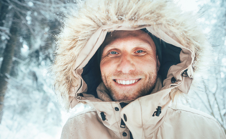 Man dressed in Warm Hooded Casual Parka Jacket Outerwear walking in snowy forest cheerful smiling face portrait.の写真素材