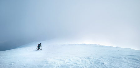 Fast going skier ride down the mountain hill into the storm clouds.の写真素材