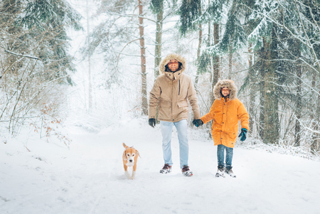 Father and son dressed in Warm Hooded Casual Parka Jacket Outerwear walking in snowy forest with his beagle dog in pine forest.の写真素材