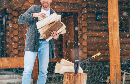 Man chopping wood on snowy yard for a house fireplace with heavy snowflakes background . Winter countryside holidays concept imageの写真素材
