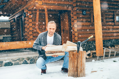 Man chopping wood on snowy yard for a house fireplace with heavy snowflakes background . Winter countryside holidays concept imageの写真素材