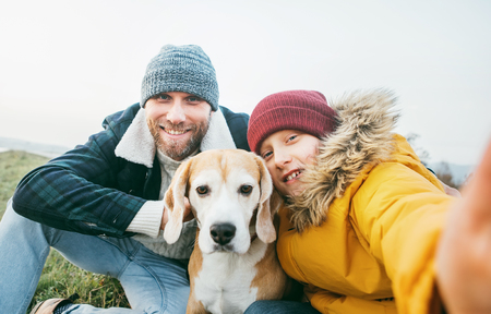 Father and son dressed in warm clothes taking a selfie photo with their best family member beagle dogの写真素材