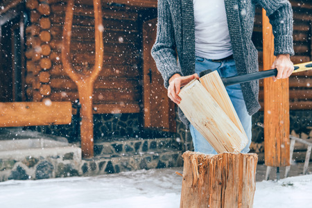 Man chopping wood on snowy yard for a house fireplace with heavy snowflakes background . Winter countryside holidays concept imageの写真素材