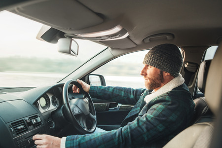 Warm dressed bearded man driving modern auto. Inside car view. Winter weather drivingの写真素材