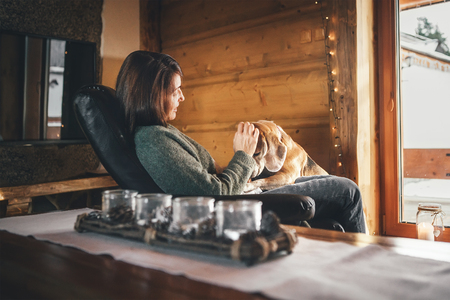 Tender scene with woman and her beagle dog  in comfortable chair opposite big window in cozy country home. Countryside vacation with pets concept image.の写真素材