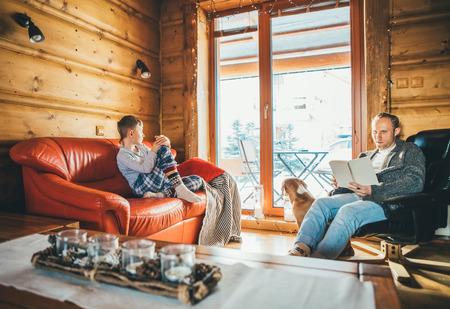 Father and son sitting on cozy couches in living room and reading. Family spending holiday time in country house concept image.の写真素材