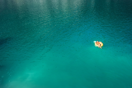 Woman swimming on inflatable pineapple ring in mountain lake top aerial view. Carefree vacation lifetime concept image.の写真素材