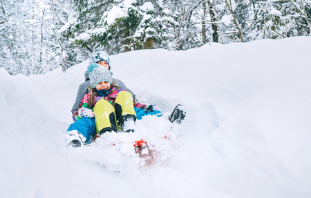 Brother and sister slide down together from snow slope in forest. Winter activities concept image.の写真素材
