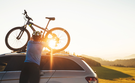 Man cyclist veared in cycling clothes and protective helmet instals his mountain bike on the car roofの写真素材