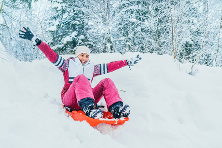 Young woman slide down from snow slope sitting in one slide.Winter activities concept image.の写真素材