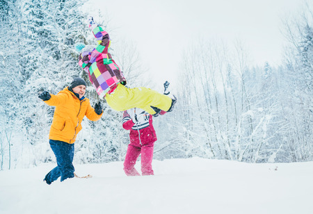 Mother and father family fooling in snow forest by throwing their little daugher to snowdriftの写真素材