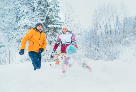 Mother and father family fooling in snow forest by throwing their little daugher to snowdriftの写真素材