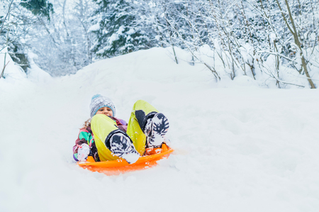 Little girl slide down from snow slope sitting in one slide.の写真素材