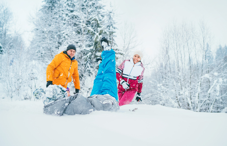 Mother and father family fooling in snow forest by throwing their little son to snowdriftの写真素材