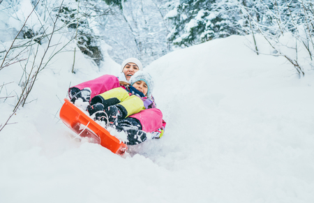Mother with daughter slide down from snow slope together sitting in one slide.Winter activities concept image.の写真素材