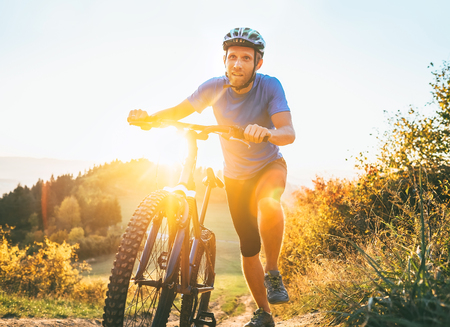 Young smiling man pushing a mountain bike up the hill. Active adventure travel on bicycle.の写真素材