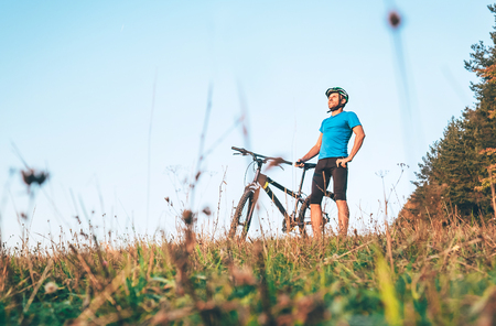 Man with bike stay on the top of hill and enjoying the sunset.の写真素材