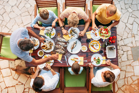 Big miltigeneration family dinner in process. Top view vertical image on table with food and handsの写真素材