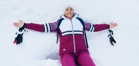 Young smiling female liying on the white snow wide opened her arms.の写真素材