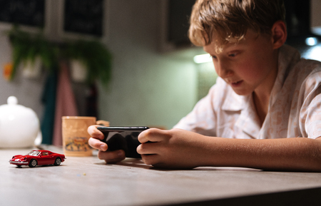 Young boy playing video game using smartphone on the kitchen table.の写真素材