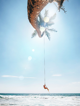 Happy little boy dangles on tropical palm tree swing. Careless happy childchood concept image.の写真素材