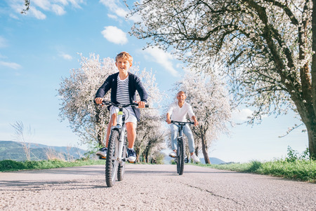 Father and son having fun when riding bicycles on country road under blossom trees. Healthy sporty lifestyle concept image.の写真素材