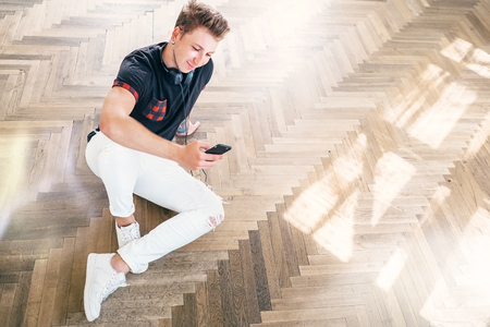 Young man using his smartphone with headphones, listen the music and sit on the floorの写真素材