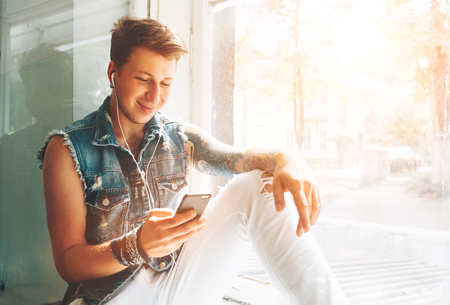 Young man listen music with headphones and smartphone sitting on windowsillの写真素材