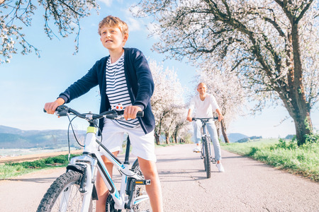 Father and son having fun when riding bicycles on country road under blossom trees. Healthy sporty lifestyle concept image.の写真素材