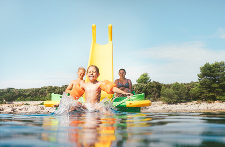 Little girl sliding down into sea water from  floating Playground slide Catamaran as she enjoying sea trip with her sister and brotherの写真素材