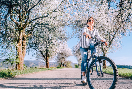 Happy smiling woman rides a bicycle on the country road under blossom trees. Spring is comming concept image.の写真素材