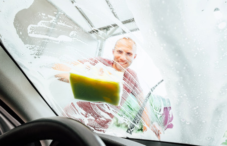 Man washing his car windshield window inside the car camera viewの写真素材