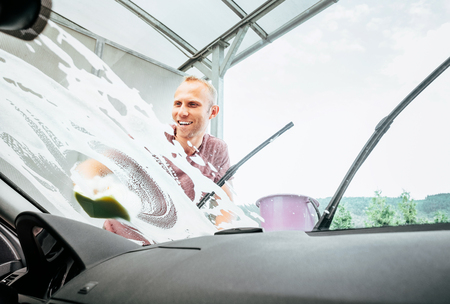 Man washes his car windshield window inside the car camera viewの写真素材