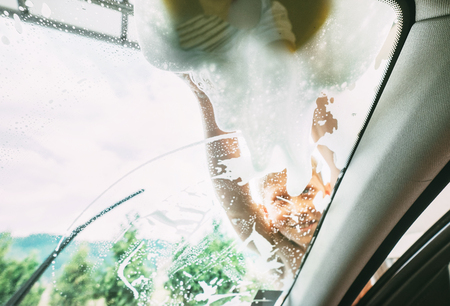 Little Boy washing his father windshield car window with soap foamy sponge. Inside car camera view.の写真素材