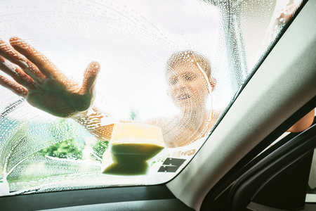Little Boy washing his family windshield car window with soap foamy sponge. Inside car camera view.の写真素材