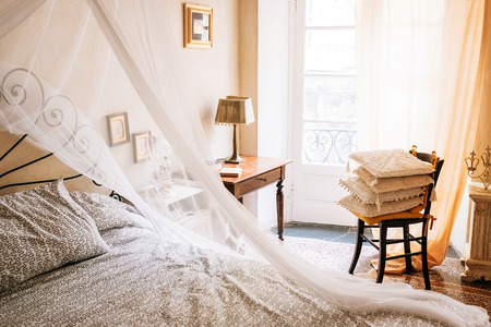 Vintage furniture retro sunny apartment with Baldachin bed, chair, cozy pillows, lamp, framed pictures on the wallsの写真素材