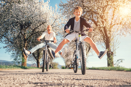 Father and son have a fun when riding bicycles on country road with blossom treesの写真素材