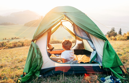 Boy rest in camping tent and enjoy with sunset light in mountain valleyの写真素材