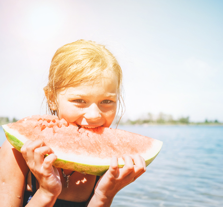 Little smiling Girl eating red watermelon portrait on the beachの写真素材