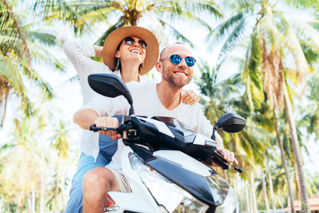 Happy smiling couple travelers riding motorbike Scooter during their tropical vacation under palm treesの写真素材