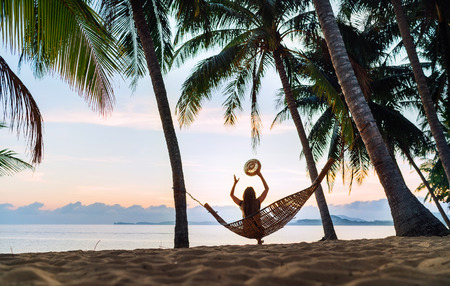 Young woman meeting sunrise sitting in hammock swinging on the exotic island sand beachの写真素材