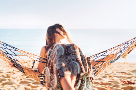 Beautiful young woman swinging in hammock hinged between palm trees and enjoying sunrise sunlight in morning time freeze frameの写真素材
