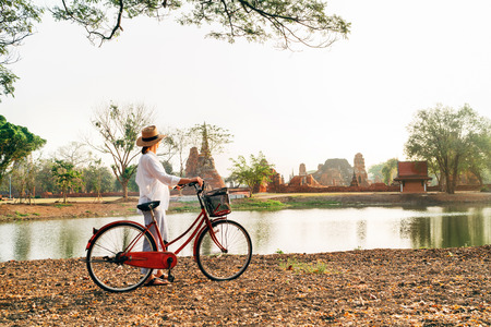 Young female traveler weared light summer clothes and hat have early morning walk with bicycle near Ayutthaya historical park in Thailand covered with morning sunlight near ancient ruinの写真素材