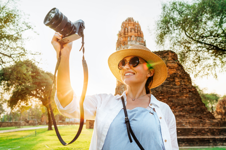 Tourist woman taking picture of ancient ruins with compact camera walking by streets of ancient Ayutthaya city, Thailandの写真素材