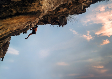 Athletic Man climbing on overhanging cliff rock with colorful sunset skyの写真素材
