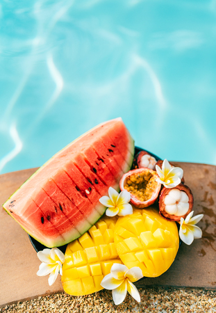 Tropical fruits and flowers still life near the pool: water melon, mango, mangosteen, passion fruitの写真素材