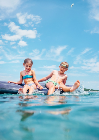 Little sister and brother sit on inflatable mattress in the sea. Happy summer holidays concept image.の写真素材